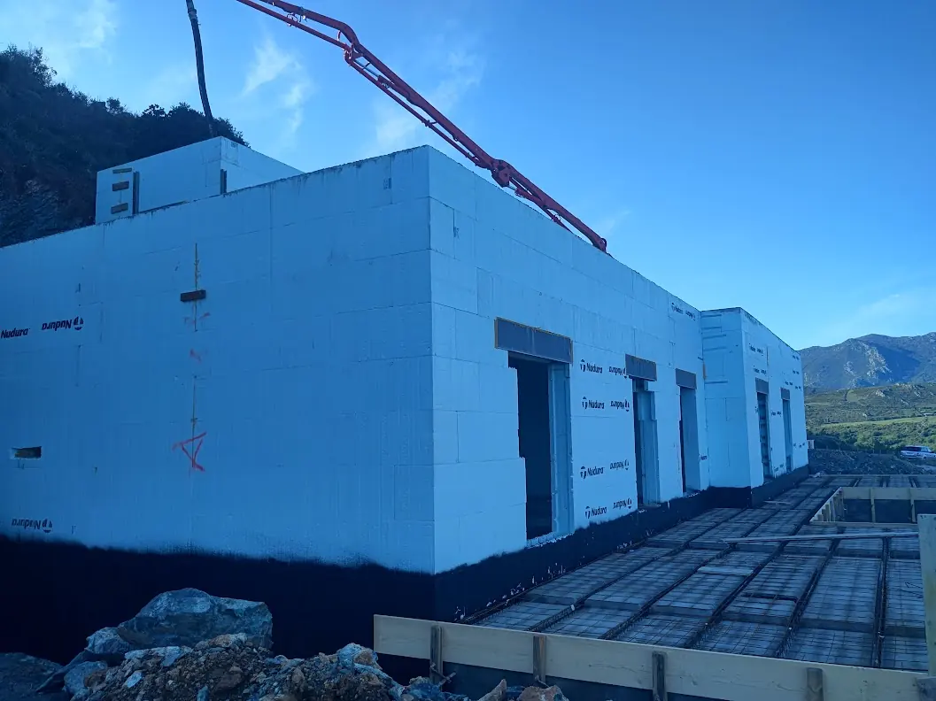 Murs Nudura montés d'une villa à Oletta, ouvertures en attente et bras de pompe à béton, face au maquis