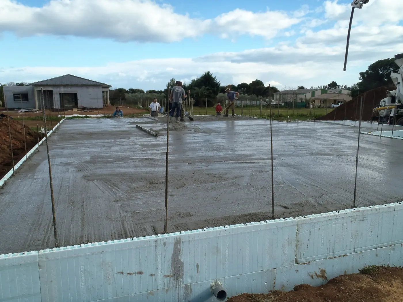 Coulage de la dalle d'une villa à Vescovato, ceinturée par le soubassement Nudura, avec une maison achevée à l'arrière-plan